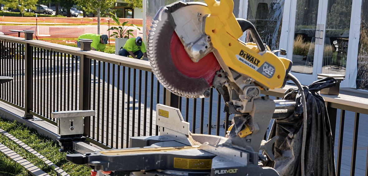 A miter saw is open and upright on a miter saw stand adjacent to a deck build in progress. 