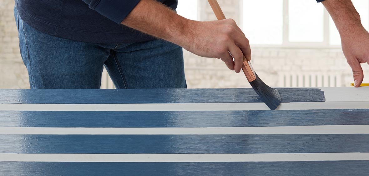 Someone uses a large flat brush to paint white PVC trim blue. 