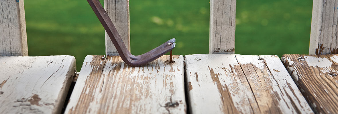 Close up of a pry bar removing nails from an old, rotting wood deck.