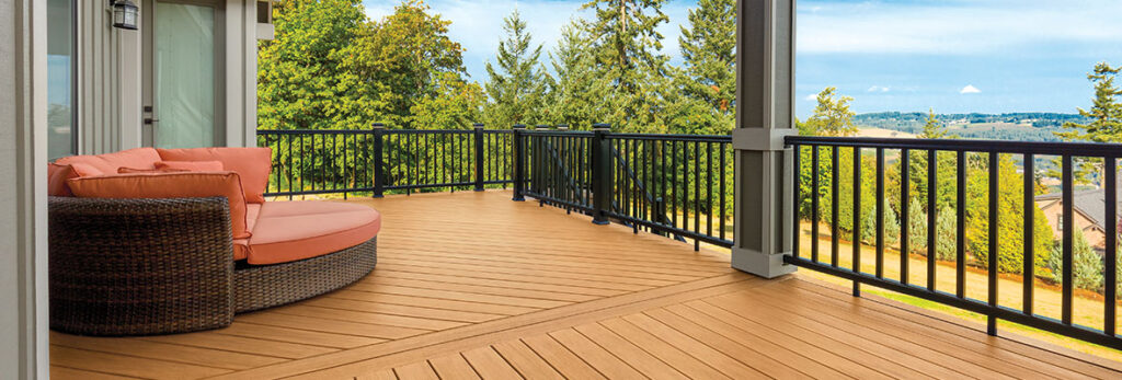 An orange loveseat on a raised composite deck shows pine trees and blue skies in the distance.