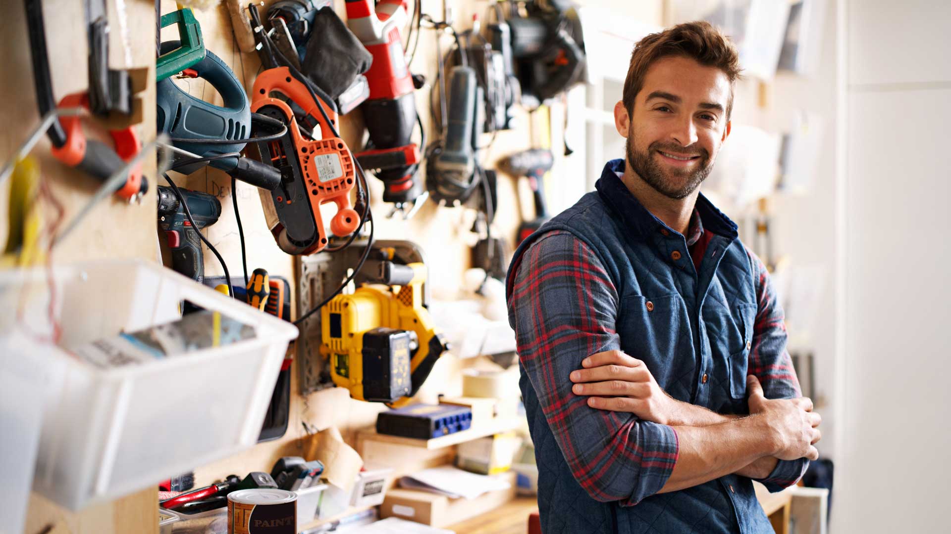 Smiling contractor in front of wall with tools hanging from it