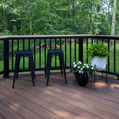 Two tone deck color schemes with two planters and two bar stools on a composite deck in a wooded area