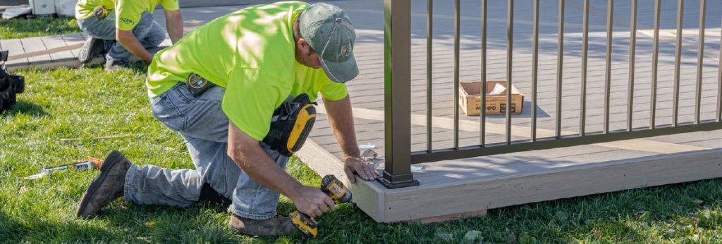 A contractor installs rim boards with a power driver to a newly installed deck.